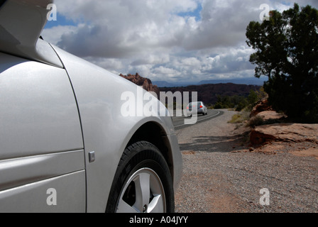 Luci di stop di accelerazione silver flash auto su come si avvicina piegare in strada, una vista parziale di argento parcheggiate auto in primo piano. Nei pressi di Moab, Utah, Stati Uniti d'America Foto Stock