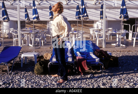 Un uomo sulla spiaggia di Nizza Francia godendo gli ultimi raggi di sole prima di prendere un volo alla fine di una vacanza Foto Stock