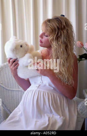 Bella donna incinta modello in abito bianco azienda orsacchiotto pensando di diventare una nuova madre Foto Stock