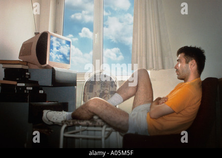 Uomo di guardare la tv da lui stesso con la finestra aperta e le nuvole riflettendo sullo schermo Foto Stock