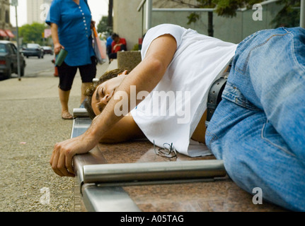 Verso il basso e fuori l'uomo a sonnecchiare su un banco del centro mentre una donna guarda a lui Foto Stock