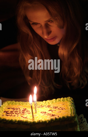 Womans viso illuminato da candele su una torta di compleanno Foto Stock