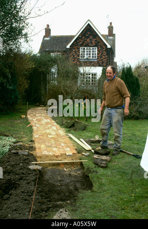 Uomo che stabilisce il percorso di mattoni sul prato in country garden Foto Stock