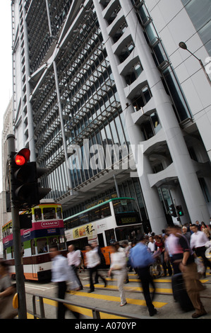 Pendolari che attraversa la strada da un tram che passa la RAS di Hong Kong e Shanghai Bank Building a Hong Kong per il distretto centrale Foto Stock