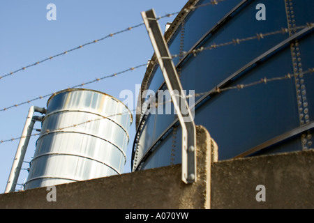 Serbatoi di acciaio in fabbrica, dietro alto filo spinato muro di sicurezza Foto Stock