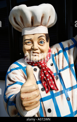 Un modello gigante chef maschio con tradizionale chef hat e abbigliamento winking e mostrando pollice in alto Foto Stock