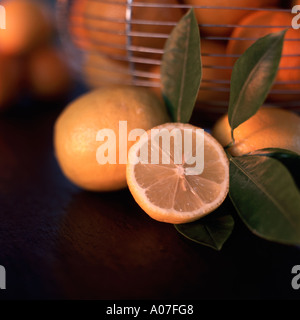 Limoni freschi interi e tagliate nella parte anteriore di un cesto in filo di arance tutti su una scheda di ardesia Foto Stock