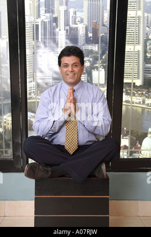 Uomo con le mani piegate che dice namaste e che fa yoga per alleviare lo stress nella sua cabina con sfondo urbano - MR Foto Stock
