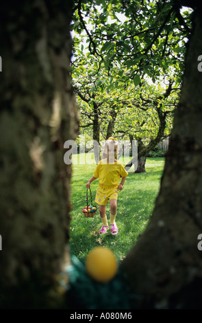 Ragazza 6 anni in esecuzione cercando uova nascoste nel cortile con la faccia felice la Domenica di Pasqua . Foto Stock