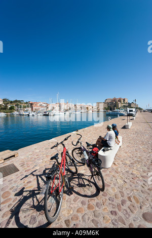 Giovane seduto sul porto con la cittadella di distanza, Calvi, La Balagne, Corsica, Francia Foto Stock