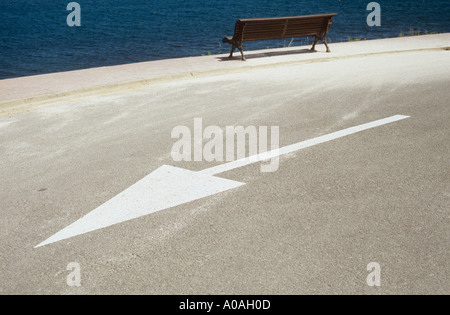 Dipinto di bianco freccia sulla strada con panca e al di là del mare Foto Stock