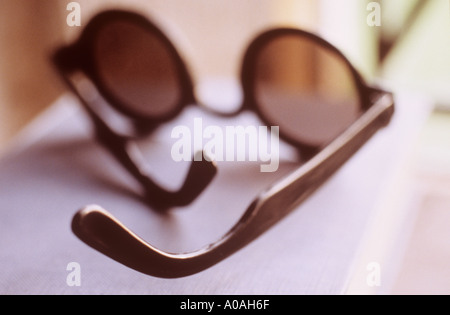 Un paio di occhiali da sole con lenti circolare giacente su un libro da una finestra Foto Stock