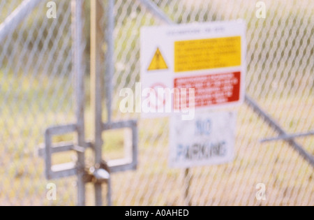 Defocussed bloccato zincata maglia di filo di recinzione con attenzione e gli avvisi di divieto e di un parcheggio non firmare Foto Stock