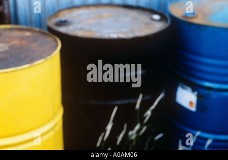 Tre olio o tamburi di chimica o lattine con qualche erba cresce attorno a loro al di fuori di un magazzino Foto Stock