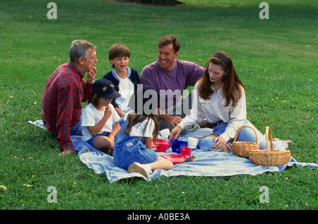 Tre generazioni di una famiglia con il nonno genitori e tre bambini seduti su una coperta avente un picnic Foto Stock