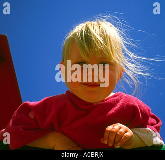 Ritratto di bambina di tre anni con i capelli biondi e cielo blu dietro con capelli soffiando nel vento Foto Stock