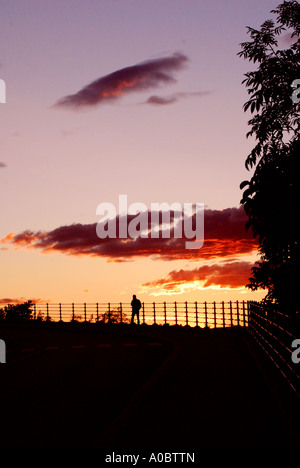 Una persona solita che si trova accanto a una recinzione ferroviaria guardando il tramonto su Oslo da un punto di osservazione a Ekeberg chiamato utsikten. Foto Stock