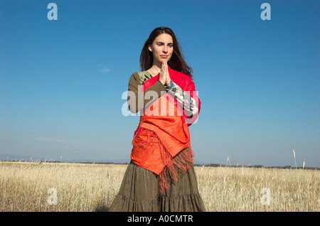 Giovane donna in piedi in campo le mani in posizione di preghiera Foto Stock