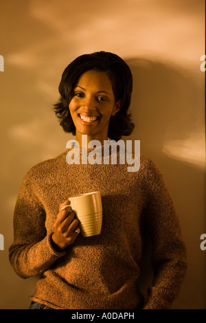Un americano africano donna gode di una tazza di caffè mentre guardando la telecamera sorridente Foto Stock