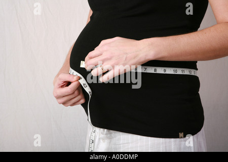 Fortemente incinta donna usa un panno nastro di misurazione per controllare la dimensione del suo crescente bump stomaco feto feto bambino closeup Foto Stock