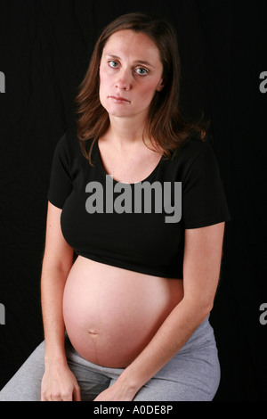 Fortemente incinta donna giovane con esposti bump dello stomaco pancia cercando indisponente premuto verso il basso in questione ormonale distante Foto Stock