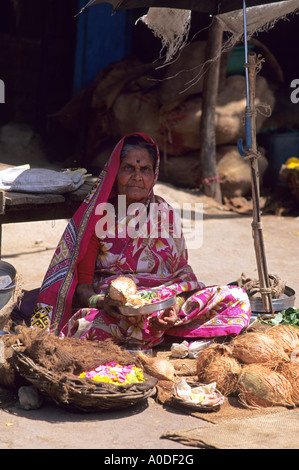 Un'anziana donna indiana venditore ambulante vendita di noci di cocco e fiori in India Foto Stock