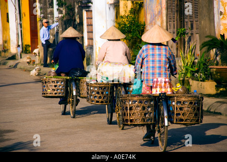 Il vietnamita ladies indossando il tradizionale cappelli conici equitazione biciclette con cesti in Hoi An, Vietnam Foto Stock