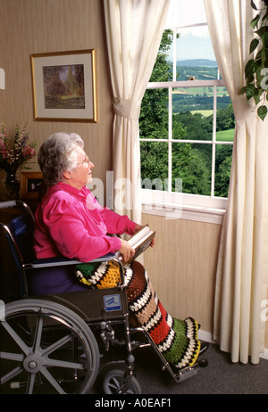 Senior donna in carrozzella a guardare fuori dalla finestra Foto Stock