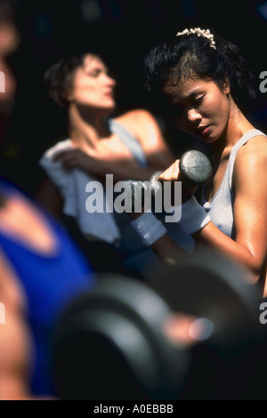 Donna asiatica con barbells sollevamento pesi mentre un'altra donna si allunga in background e uomo ascensori barbell in primo piano Foto Stock