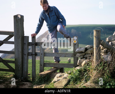 DORSET UK ottobre una donna salendo un di legno stile sul sud-ovest sentiero costiero con la scogliera dietro Foto Stock