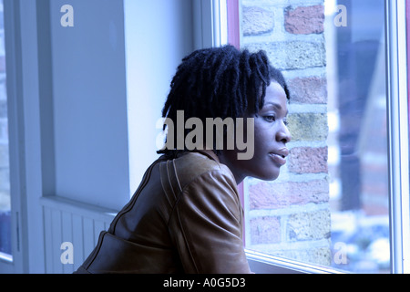 Nero donna guardando fuori da una finestra Foto Stock