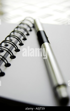 Libro bianco con rilegatura a spirale nera, penna in acciaio inox. Sparato su un piano da tavolo in acciaio inox funky punzonato. Foto Stock