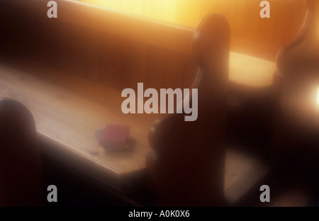 Pressione atmosferica semplice chiesa di legno banchi con un rosso e un libro blu giacente su un sedile e golden dietro alla luce del sole Foto Stock