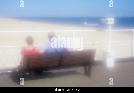 Pressione atmosferica vista da dietro del giovane seduto su un banco di lavoro sul molo o promenade guardando ampia spiaggia di sabbia e il blu del mare e del cielo Foto Stock