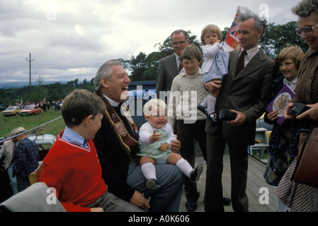 Politico che tiene in braccio un bambino infelice che piange al raduno politico il Rev. Ian Paisley ridendo, felice Ballymoney Irlanda del Nord anni '1980 Regno Unito 1981 HOMER SYKES Foto Stock