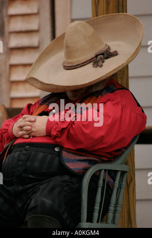 Cowboy in maglietta rossa e sombrero seduto e dormire sul lungomare di una città vecchia Foto Stock