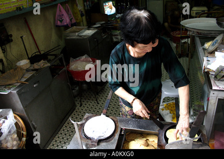 La donna in una piccola strada shop rende piccoli pancake deserto su una padella, Macau, SAR Foto Stock
