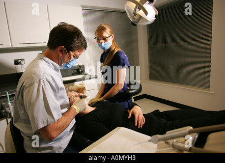 Denti e gomma di trattamento da parte di un medico dentista e il suo assistente in un paziente in una sedia dentisti in una chirurgia dentale Foto Stock