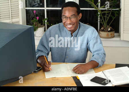 Uomo in ufficio a casa facendo il suo imposte, contabilità o di contabilizzazione e sorridente Foto Stock