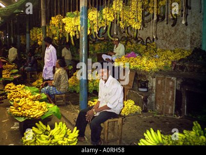 Uomo sorridente uomo vendere sit resto in animate colorato occupato tradizionali di banane sul mercato di frutta Mysore Karnataka India Asia del Sud Foto Stock