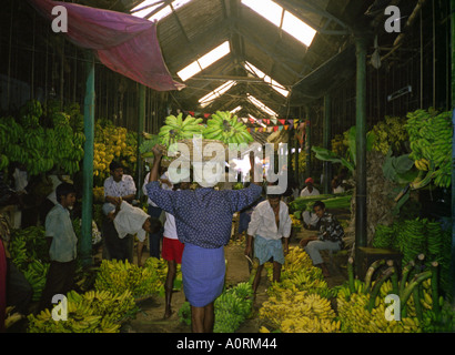 Uomini uomo trasportare pesanti cesto di paglia sulla testa in animate colorato banana affollato mercato della frutta Mysore Karnataka India Asia del Sud Foto Stock