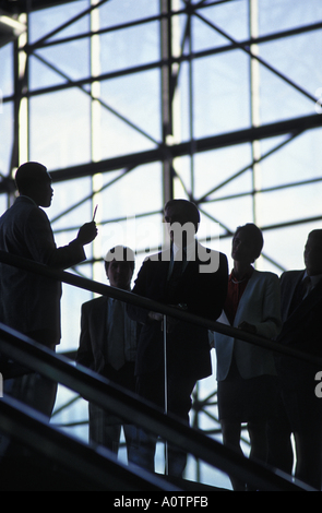 Silhouette di un gruppo di dipendenti di essere indirizzata da un mentor in un atrio protetto da vetro Foto Stock