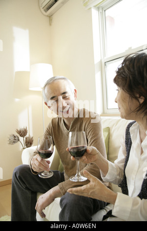 Coppia senior seduto su un divano e tenendo i bicchieri di vino rosso Foto Stock