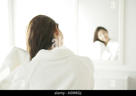 Vista posteriore di una giovane donna asciugando i capelli con un asciugamano davanti a uno specchio Foto Stock