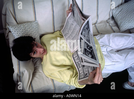 Una donna thirites sorrisi come si guarda da un divano mentre leggendo un giornale Foto Stock