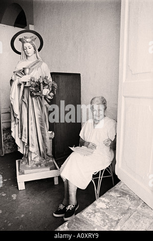 Signora anziana insediato dalla finestra a casa e la grande statua della Vergine Maria. Trinidad, Cuba Foto Stock