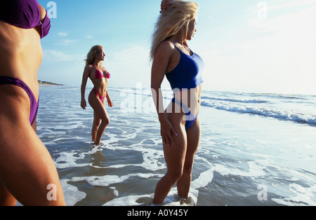 Profilo laterale di tre giovani donne che indossano Bikini sulla spiaggia Foto Stock