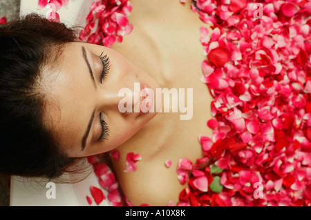 Angolo di alta vista di una giovane donna reclinata in una vasca da bagno piena di petali di rosa Foto Stock