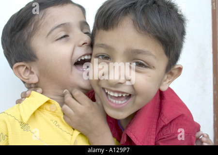 Due ragazzi indiani kids bambini sorridenti ridere giocando scherzi abbracciando il divertimento di condivisione divertente scherzo felice denti shirt rosso giallo Foto Stock