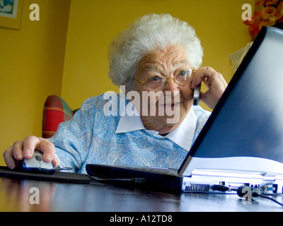 Schermo di computer telefono cellulare anziani vivace senior lady è affascinato dalla sua lo schermo del computer portatile durante la conversazione sul suo telefono cellulare Foto Stock